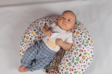 Portrait of a two month old boy looking at camera cutely and smiling as he sleeps in brown clothes in newborn baby photo shoot
