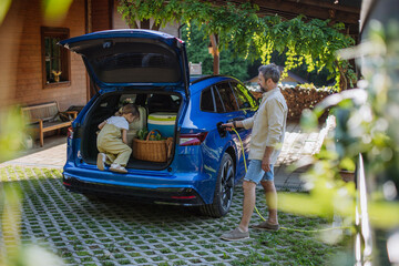 Wall Mural - Father charging their electric car, little daughter sitting and waiting in a car trunk.