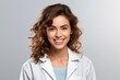 smiling young female doctor in white coat looking at camera isolated on grey