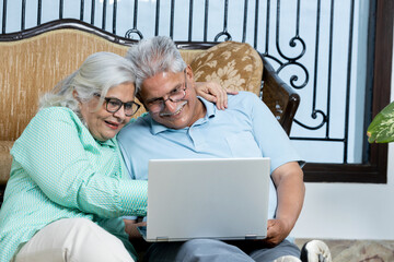 indian senior couple with laptop sitting on floor at Living room