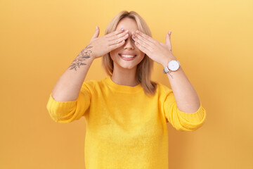 Wall Mural - Young caucasian woman wearing yellow sweater covering eyes with hands smiling cheerful and funny. blind concept.