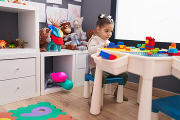 Wall Mural - Adorable hispanic girl playing with construction blocks sitting on table at kindergarten