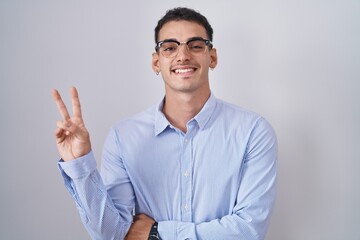 Poster - Handsome hispanic man wearing business clothes and glasses smiling with happy face winking at the camera doing victory sign. number two.