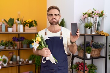 Sticker - Middle age man with beard working at florist shop showing smartphone screen puffing cheeks with funny face. mouth inflated with air, catching air.