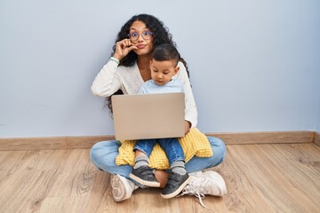 Poster - Young hispanic mother and kid using computer laptop sitting on the floor mouth and lips shut as zip with fingers. secret and silent, taboo talking