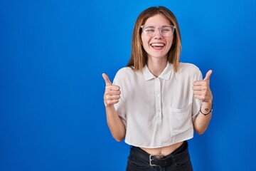 Sticker - Beautiful woman standing over blue background success sign doing positive gesture with hand, thumbs up smiling and happy. cheerful expression and winner gesture.