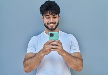 Wall Mural - Young hispanic man smiling confident using smartphone over white isolated background