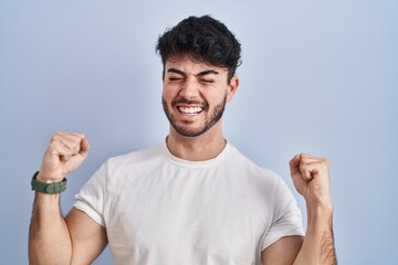 Wall Mural - Hispanic man with beard standing over white background celebrating surprised and amazed for success with arms raised and eyes closed. winner concept.