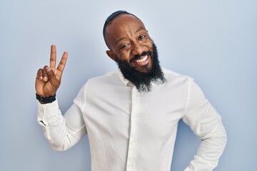 Poster - African american man standing over blue background smiling looking to the camera showing fingers doing victory sign. number two.