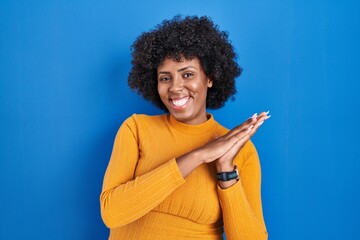 Poster - Black woman with curly hair standing over blue background clapping and applauding happy and joyful, smiling proud hands together