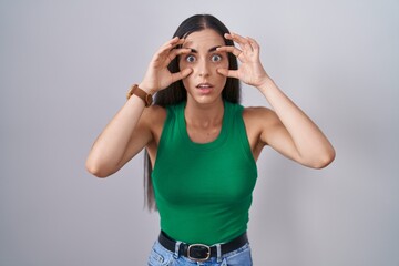 Wall Mural - Young woman standing over isolated background trying to open eyes with fingers, sleepy and tired for morning fatigue