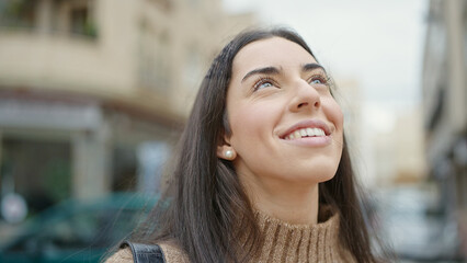 Wall Mural - Young beautiful hispanic woman smiling confident looking to the sky at street