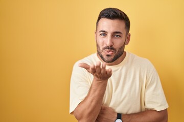 Canvas Print - Handsome hispanic man standing over yellow background looking at the camera blowing a kiss with hand on air being lovely and sexy. love expression.