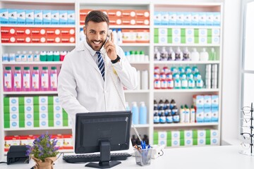 Poster - Young hispanic man pharmacist talking on telephone using computer at pharmacy