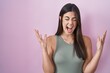 © Krakenimages.com - Hispanic woman standing over pink background celebrating mad and crazy for success with arms raised and closed eyes screaming excited. winner concept