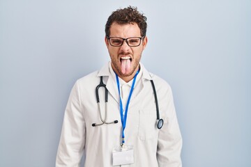 Sticker - Young hispanic man wearing doctor uniform and stethoscope sticking tongue out happy with funny expression. emotion concept.