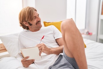 Poster - Young blond man writing on notebook lying on bed at bedroom