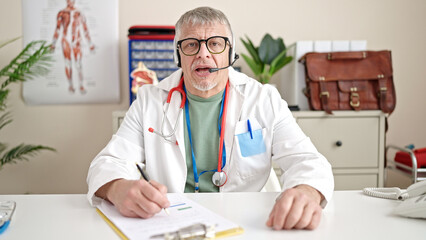 Poster - Middle age grey-haired man doctor having online medical consultation at clinic