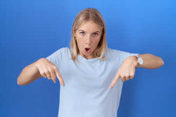 Poster - Young caucasian woman wearing casual blue t shirt pointing down with fingers showing advertisement, surprised face and open mouth