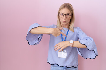 Poster - Young caucasian business woman wearing id card in hurry pointing to watch time, impatience, upset and angry for deadline delay