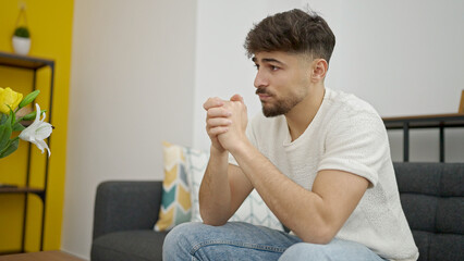 Wall Mural - Young arab man sitting on sofa with relaxed expression at home