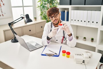 Sticker - Young arab man wearing doctor uniform analysing urine test tube speaking at clinic