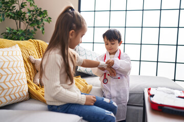 Adorable boy and girl wearing doctor uniform bandaging arm at home