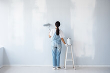 A Woman In Denim Overalls Paints A Wall With A Roller. Photorealistic Illustration Of Generative AI.