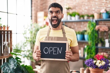 Canvas Print - Hispanic man with beard working at florist holding open sign angry and mad screaming frustrated and furious, shouting with anger looking up.