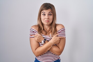 Young hispanic woman standing over isolated background pointing to both sides with fingers, different direction disagree