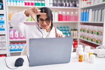 Wall Mural - Young arab woman working at pharmacy drugstore using laptop smiling making frame with hands and fingers with happy face. creativity and photography concept.