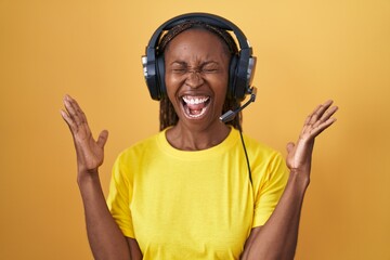 Canvas Print - African american woman listening to music using headphones celebrating mad and crazy for success with arms raised and closed eyes screaming excited. winner concept