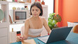 © Krakenimages.com - Young beautiful hispanic woman using laptop sitting on table at dinning room