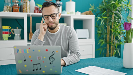 Sticker - Hispanic man talking on smartphone using laptop at dinning room