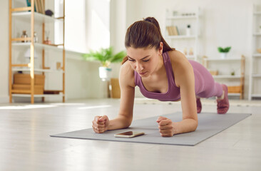 beautiful fit young woman having sports workout at home, doing plank exercise on yoga mat, trying to