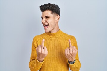 Canvas Print - Young hispanic man standing over blue background showing middle finger doing fuck you bad expression, provocation and rude attitude. screaming excited