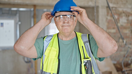 Poster - Middle age grey-haired man builder smiling confident wearing hardhat at construction site