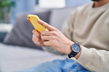 Sticker - Young arab man using smartphone sitting on sofa at home