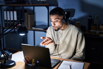 Poster - Young handsome man working using computer laptop at night looking at the camera blowing a kiss with hand on air being lovely and sexy. love expression.