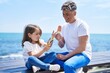 Father and daughter eating ice cream sitting on bench at seaside