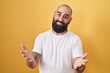 © Krakenimages.com - Young hispanic man with beard and tattoos standing over yellow background smiling cheerful offering hands giving assistance and acceptance.