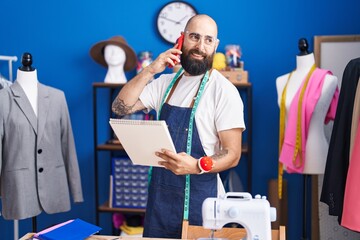 Poster - Young bald man tailor talking on smartphone looking clothing design at clothing factory