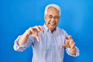 Sticker - Hispanic senior man wearing glasses smiling funny doing claw gesture as cat, aggressive and sexy expression