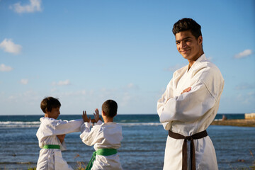 Teacher training children in karate and traditional martial arts. Simulation of fight near the sea. Portrait of instructor with boys in background