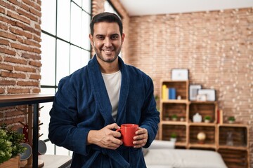 Wall Mural - Young hispanic man wearing robe drinking coffee at home