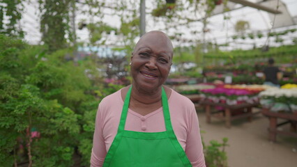 One Happy African American senior woman wearing green apron standing inside Flower Shop looking at camera smiling