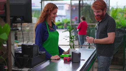 Wall Mural - Male Customer Purchasing Plant with contactless payment cellphone at Horticulture Store Checkout. Female employee Assisting Client at Local Business