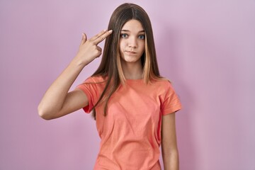 Sticker - Teenager girl standing over pink background shooting and killing oneself pointing hand and fingers to head like gun, suicide gesture.