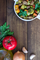 Wall Mural - beef meat stewed with potatoes, carrots and spices in ceramic pot with ingredients on wooden background. vertical