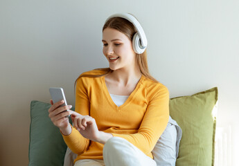 Wall Mural - Young Woman With Earphones Using Smartphone Listening Music In Bedroom